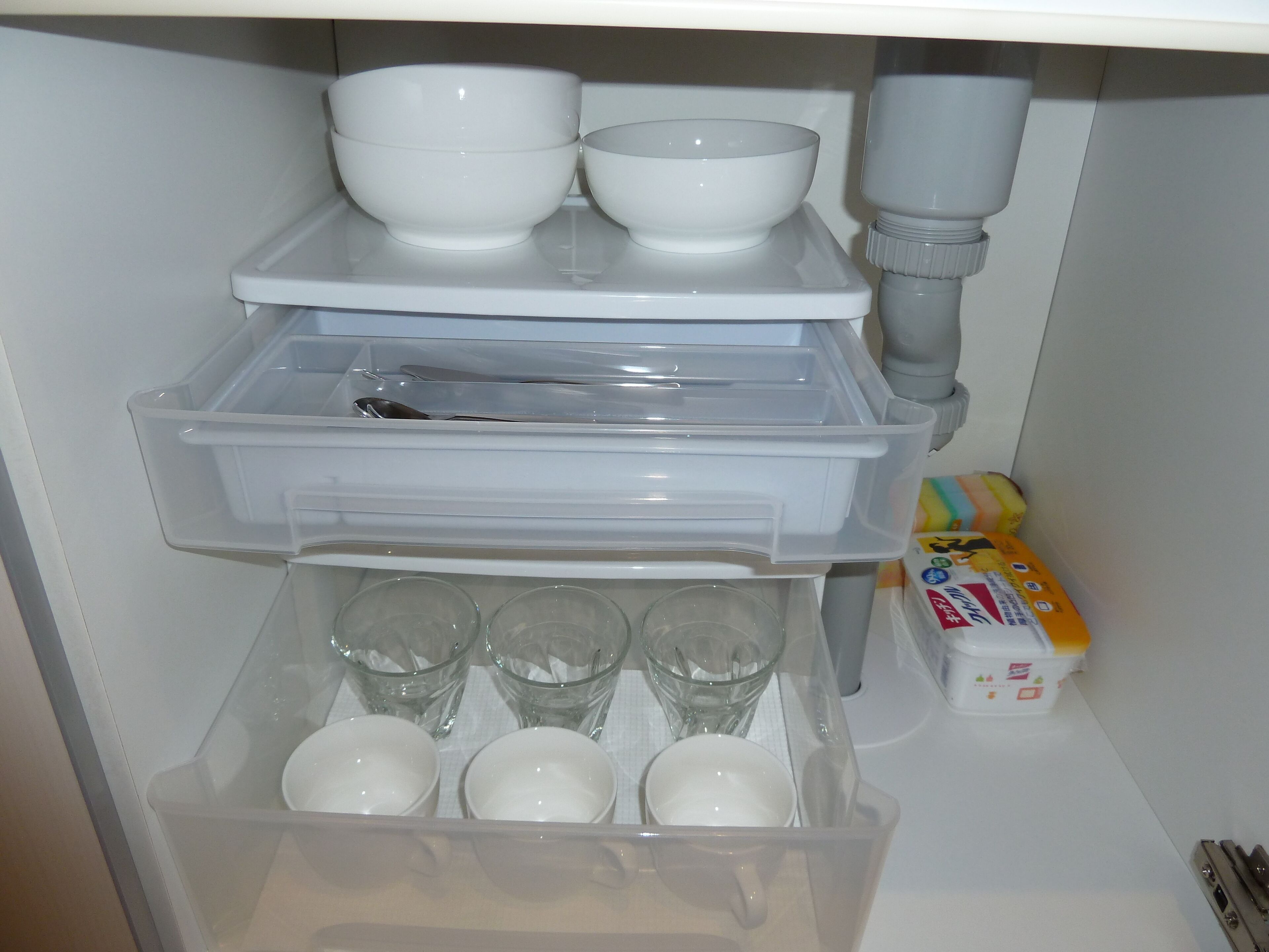 A kitchen with a built-in dishwasher, a sink, and a storage area with clear glasses and a box of tissues.