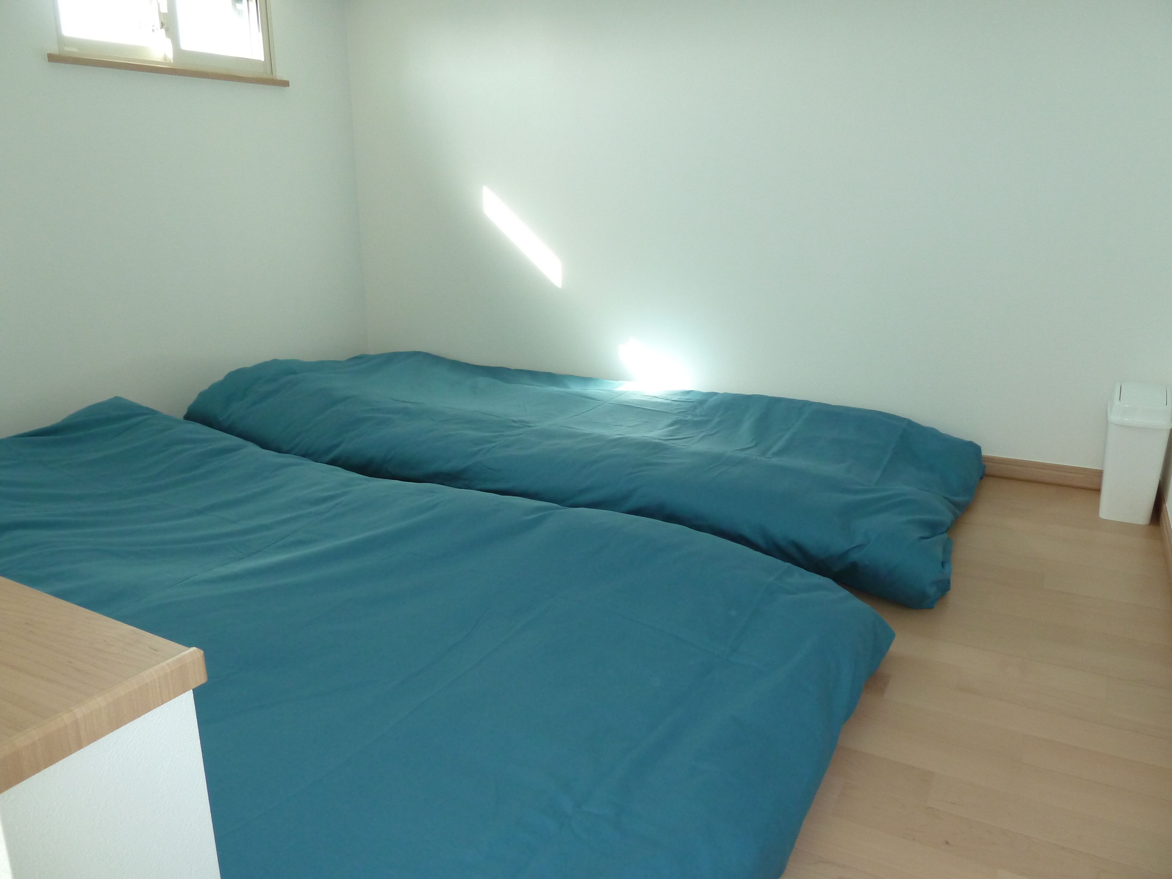 Quarto com duas camas, uma janela e uma lixeira branca.