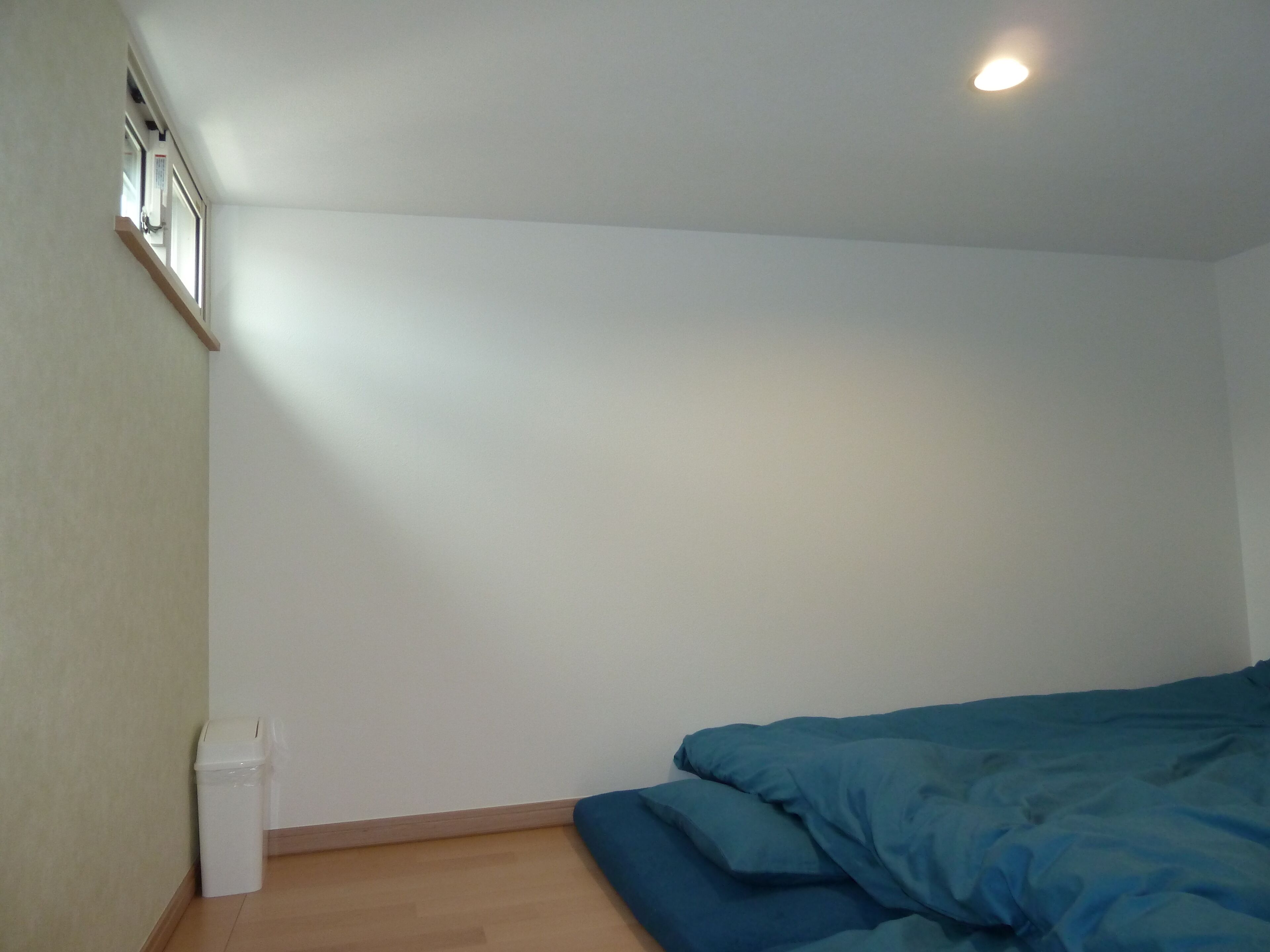 Une chambre avec un lit simple, une petite poubelle et une fenêtre.