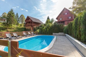 Una piscina con sillones de descanso, rodeada de cabañas de madera y árboles.