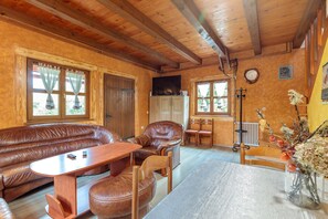 Ein gemütliches Zimmer mit Holzbalkendecke, Ledersofa, Holztisch und einer Vase mit Blumen.