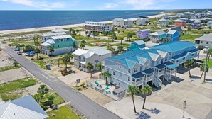 Un quartier résidentiel situé sur la côte, avec de nombreuses maisons à deux étages, dont certaines ont des toits bleus, et une plage en arrière-plan.