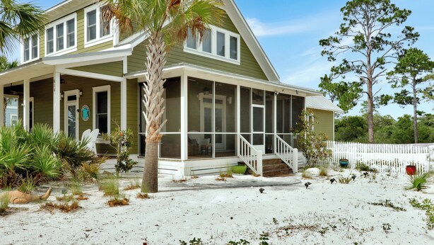 A two-story house with a covered porch, a fenced yard, and a sandy beach in front. - ☀️ Pet Friendly - Secluded Beach Cottage - Four Winds Cottage 🌴 (St Joe Beach)