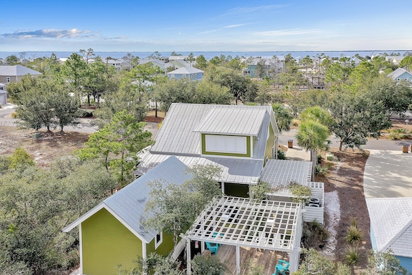 Houses with unique architectural styles are surrounded by lush greenery and a distant sea view.