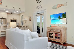 A living room with a white sofa, wooden cabinets, a television displaying a beach scene, and a fish decoration on the wall.