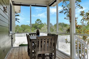 A covered porch with a table and chairs, a white railing, and a view of trees and sky.