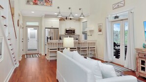 A spacious living area with a white sofa, a dining table, and a kitchen with white cabinets and stainless steel appliances. - ☀️ Pet Friendly - Secluded Beach Cottage - Four Winds Cottage 🌴 (St Joe Beach)