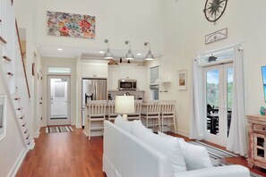 A spacious living area with a white sofa, a dining table, and a kitchen with white cabinets and stainless steel appliances.