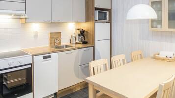 A modern kitchen with white cabinetry, a built-in oven, a coffee maker, and a dining area with a table and chairs.