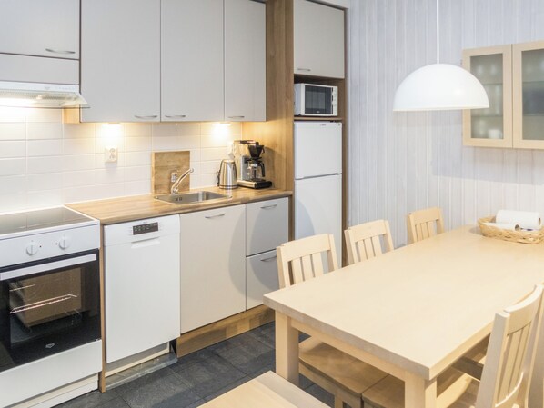 Una cocina moderna con armarios blancos, horno integrado, cafetera y comedor con mesa y sillas.