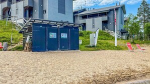 A modern building with a blue exterior, a small blue structure with signs, and a sandy beach area with red lounge chairs. - Rukatonttu d 15 by Interhome (Kuusamo)