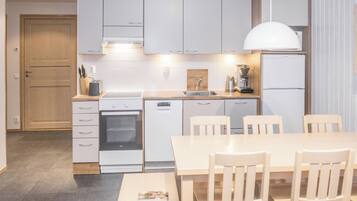 A modern kitchen with white cabinets, a built-in oven, a coffee machine, and a dining table with chairs.