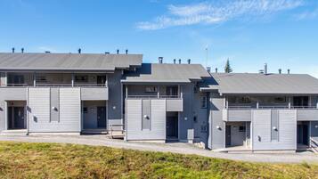 A row of modern, grey buildings with flat roofs, likely residential or office units, with a clear sky above.