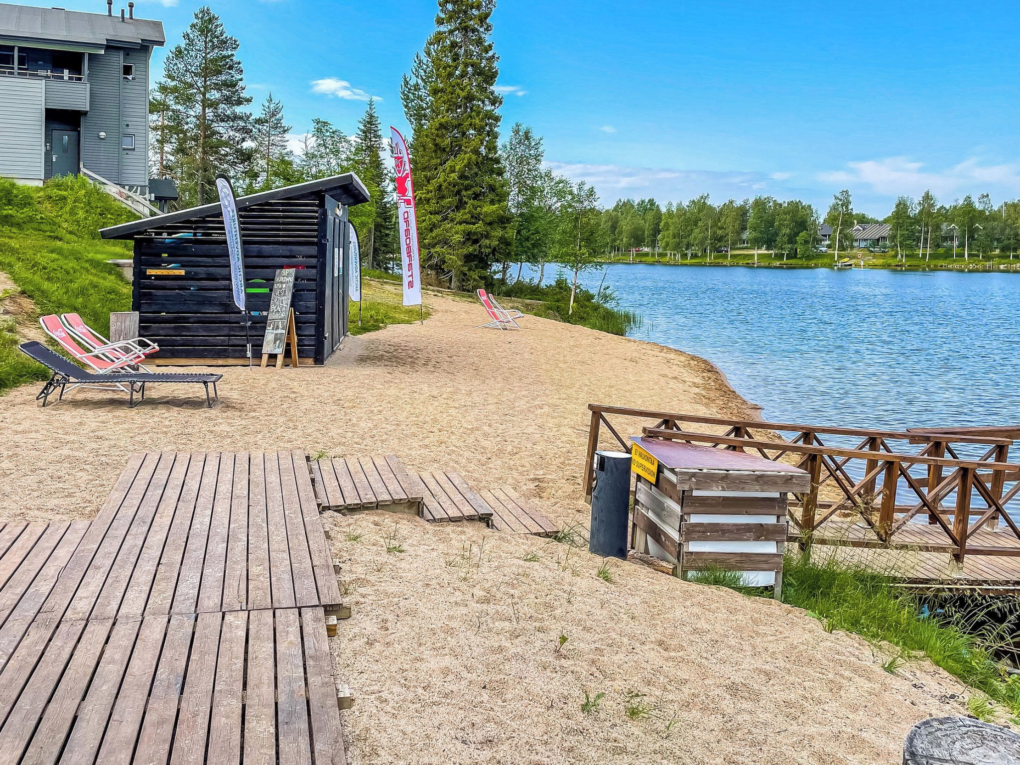 A lakeside wooden deck with lounge chairs, a small wooden structure, and a dock extending into the water.