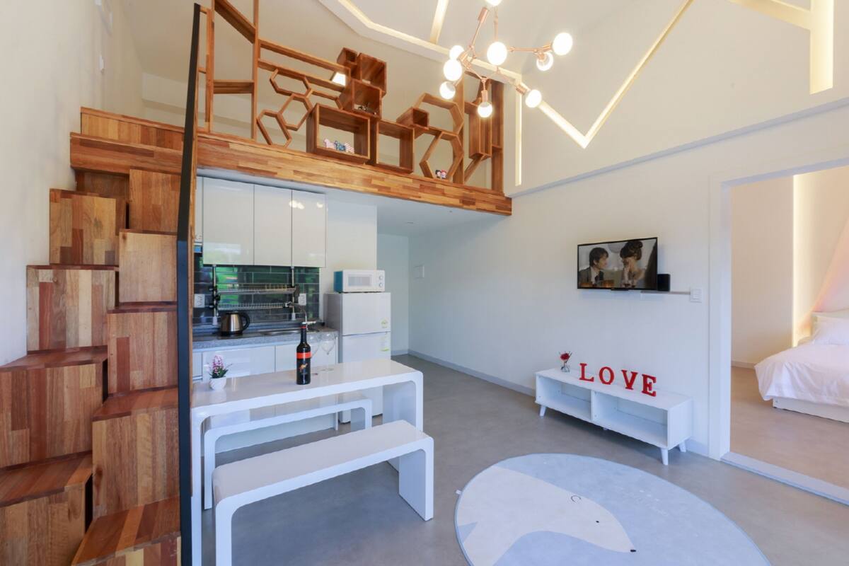 Une chambre d’hôtel moderne avec un escalier en bois, un coin cuisine, un espace salon et un lit.