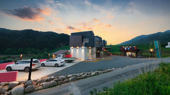 A modern building with a flat roof and a large entrance. There are two white cars parked in front. - Gyeongju Edith Poolvilla & Pension (Gyeongju)