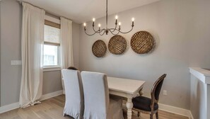 Uma sala de jantar com mesa branca, duas cadeiras, um lustre e três decorações de parede em tecido.