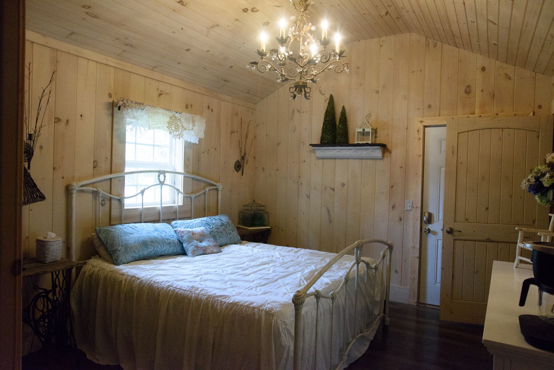 Ein Zimmer aus Holz mit einem Bett, einer Kristallleuchtre, einer Tür und einem kleinen Regal mit Dekoration.