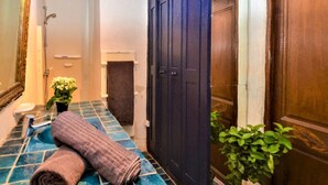 Un baño con piso de baldosas azules, una toalla, una planta y una puerta de madera oscura.