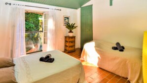 Una habitación con dos camas, una ventana con cortinas, una planta sobre una cómoda y una puerta.