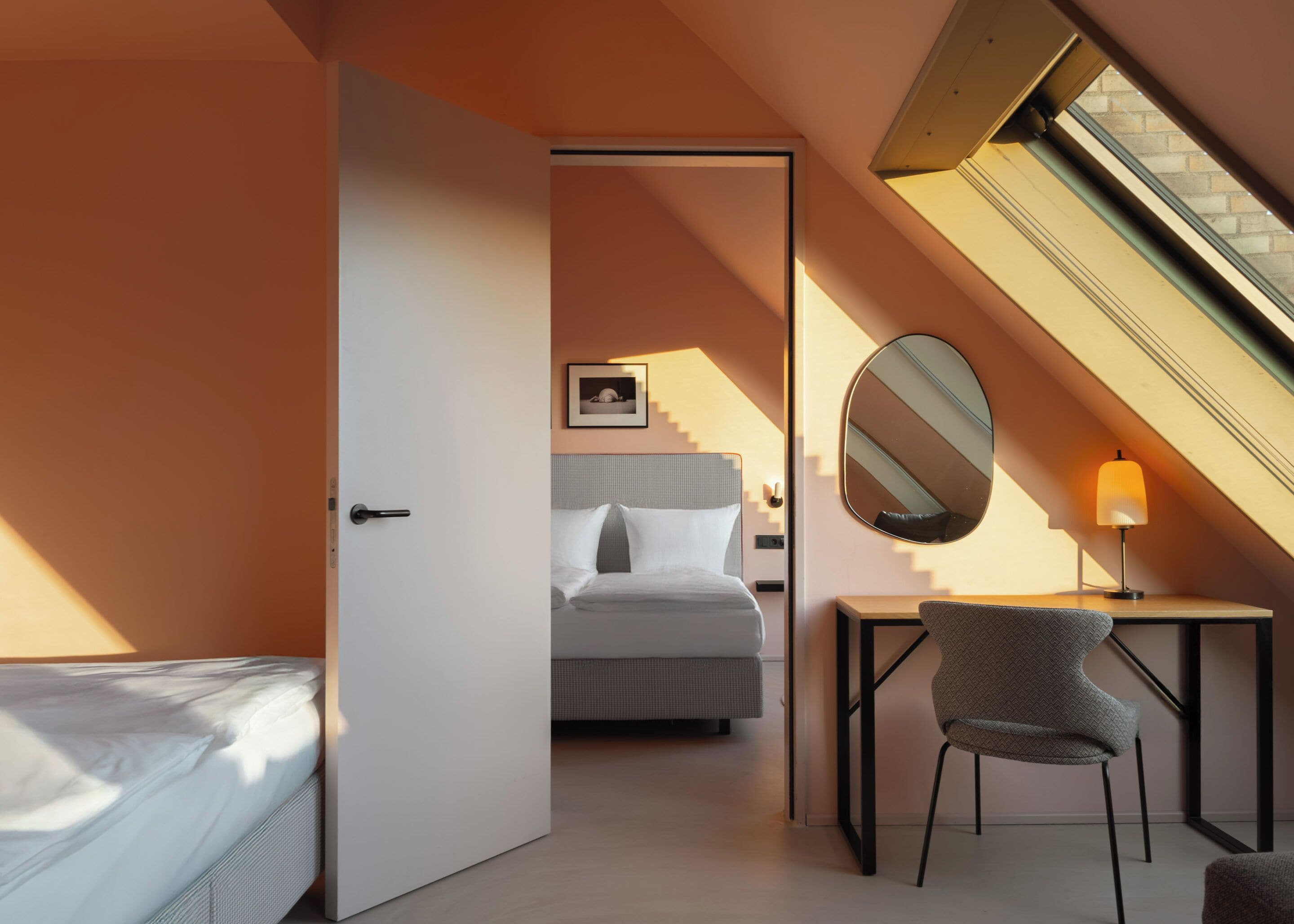 Een moderne slaapkamer met een bed, een bureau, een stoel, een spiegel en een trap naar een hoger gelegen verdieping.
