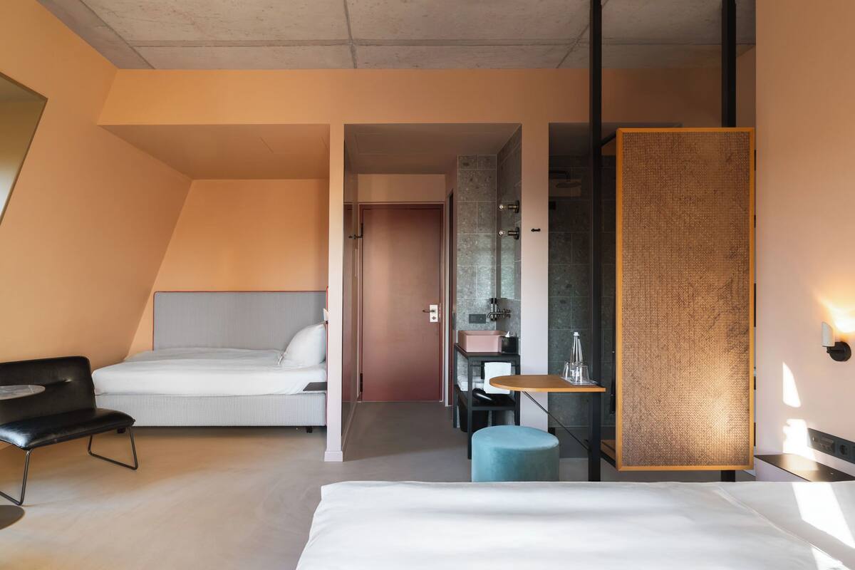 A modern hotel room with a large bed, a small desk, a chair, and a bathroom visible through an open door.
