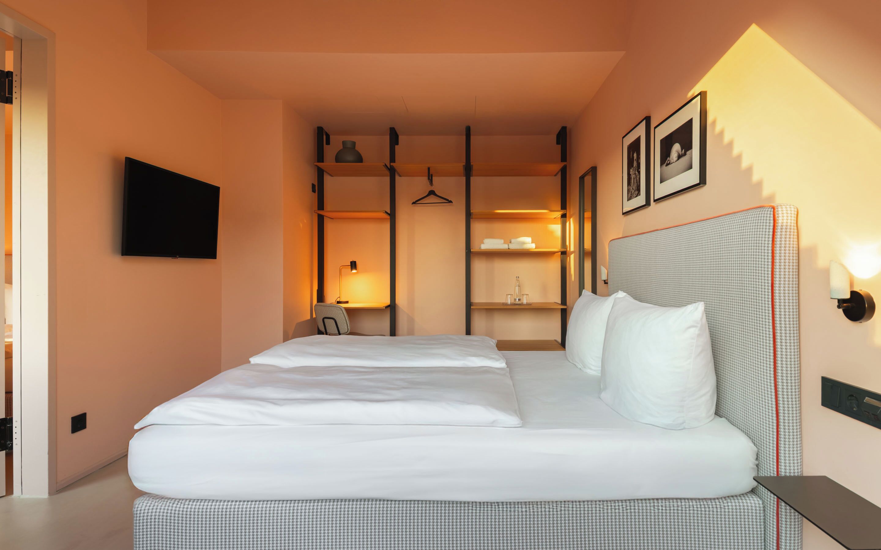 A hotel room with a large bed, a TV mounted on the wall, and a wardrobe with shelves.
