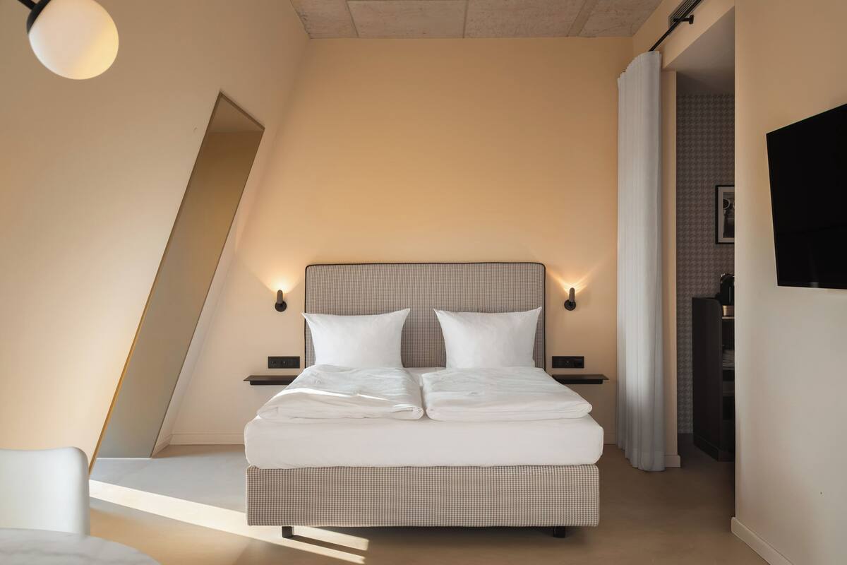 A modern bedroom with a large bed, two bedside tables, a wall-mounted TV, and a ceiling light.