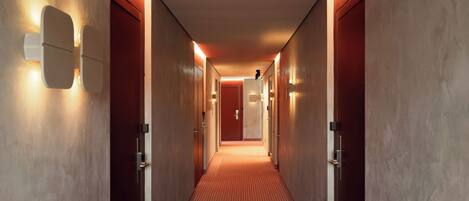 Un pasillo con alfombra estampada, puertas de madera y luminarias fijadas a la pared.