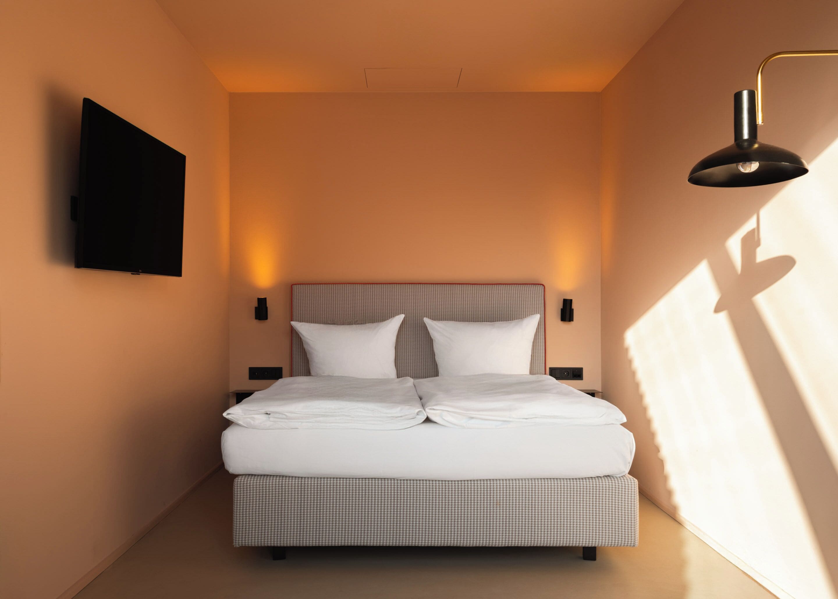 Una cama bien hecha con cabecera, mesitas de noche y un televisor fijado a la pared.