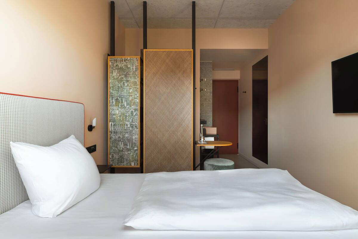 A hotel room with a bed, a large mirror, a small table, and a wall-mounted TV.