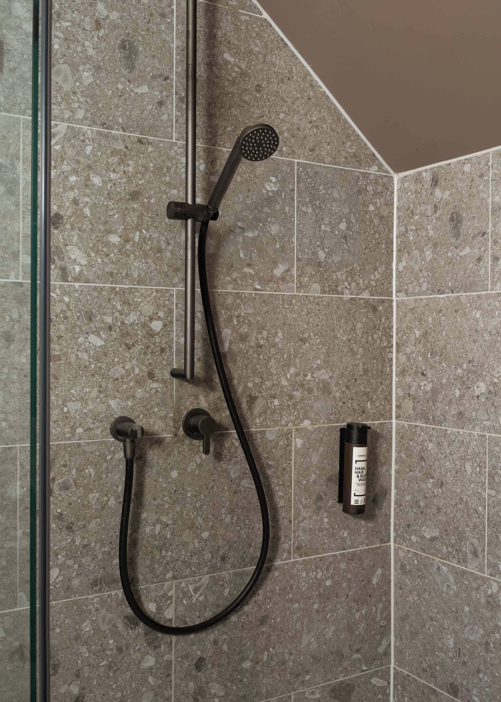 A shower area with a handheld showerhead, a handheld shower hose, and a bottle of hand soap.
