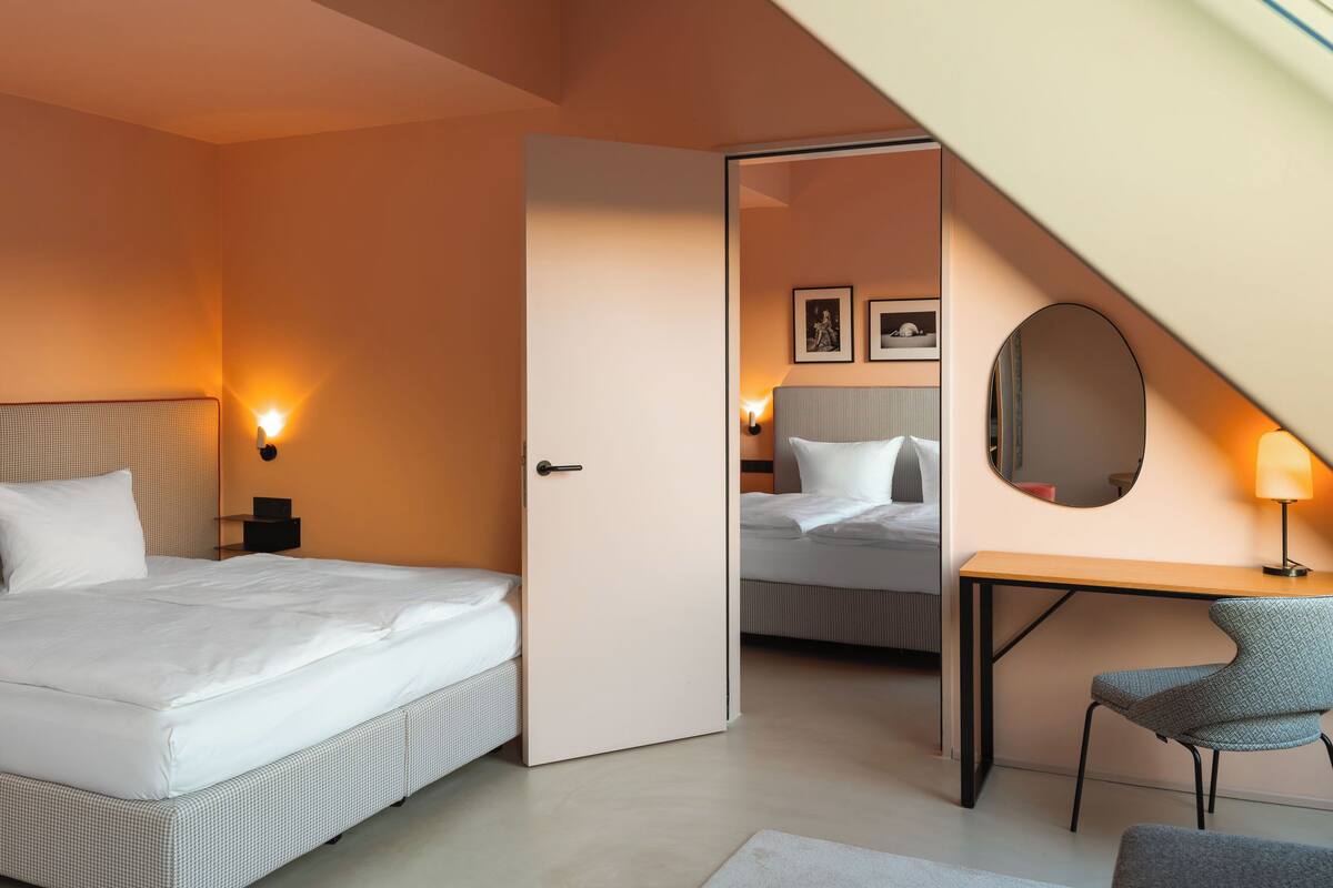 A hotel room with a bed, bedside table, lamp, chair, and a mirror on the wall.