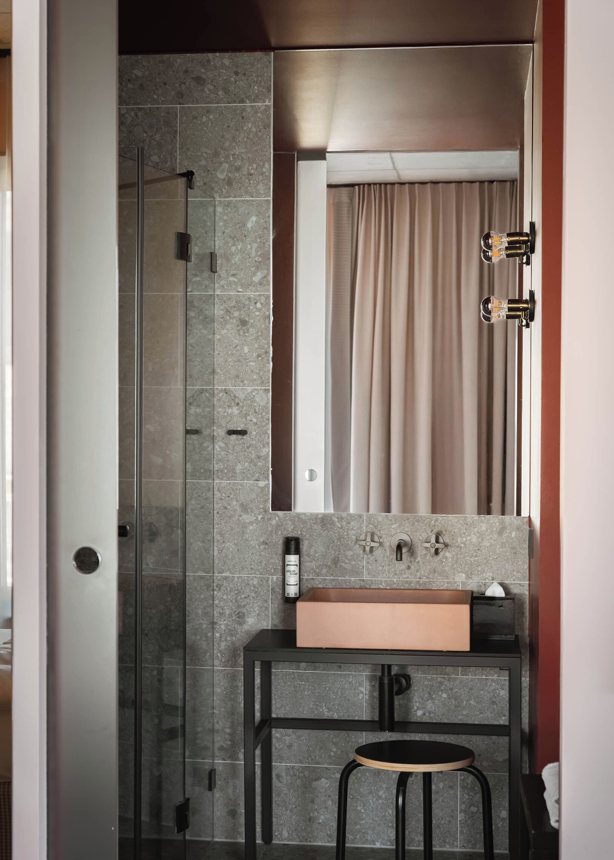 Une salle de bain moderne avec une douche à parois de verre, un lavabo avec un miroir au-dessus et un tabouret.