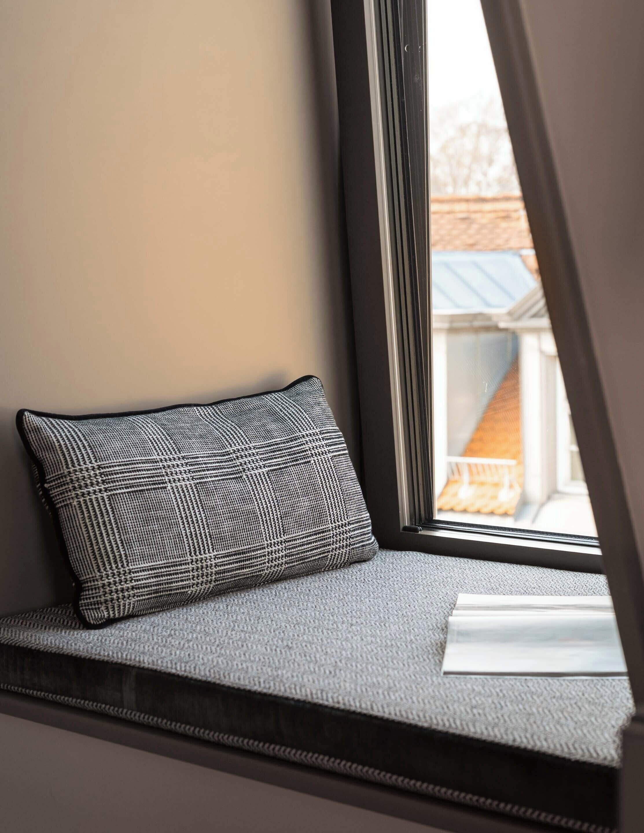Assento junto à janela com almofada estampada e vista para um edifício.