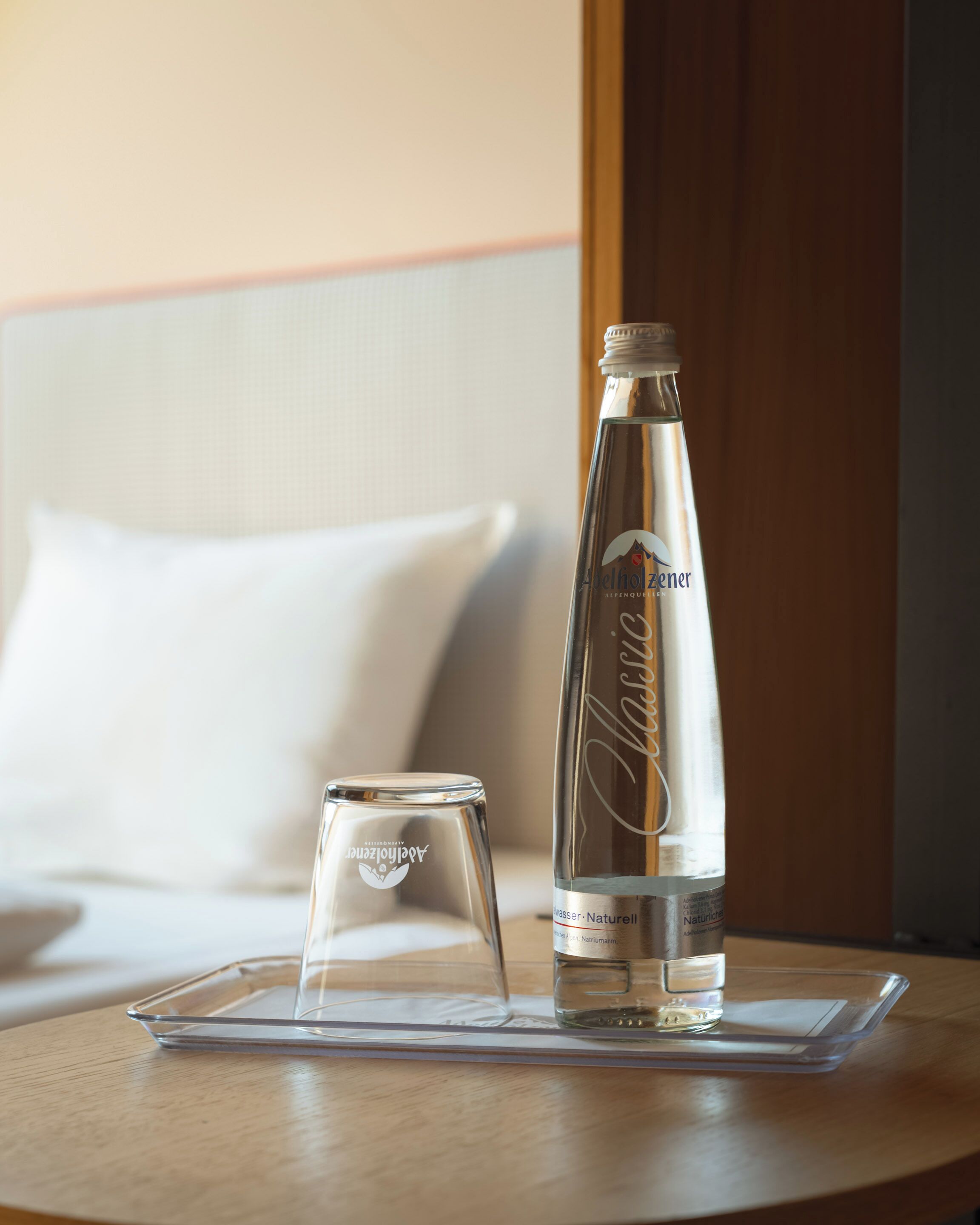 Eine Flasche Alpelholzer Bier und ein Glas auf einem klaren Untersetzer auf einem Holztisch in einem Hotelzimmer.