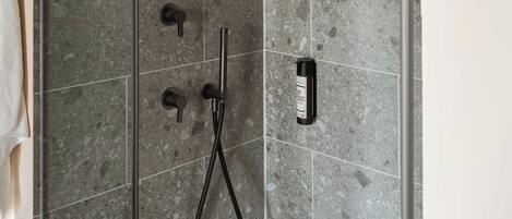 A shower area with a handheld showerhead and a handheld hose.