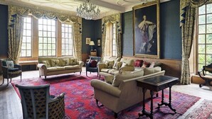 Een luxueuze kamer met een gedetailleerd plafond, grote ramen en klassiek meubilair.