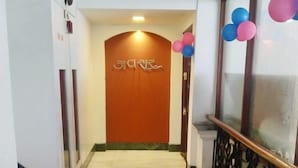 A hallway with a marble floor, a wooden door with a sign, and a railing with balloons. - Hotel Yuvraj (Vadodara)