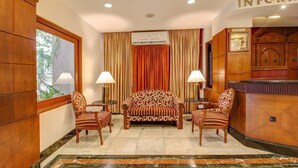 A hotel lobby with a sofa, two armchairs, a reception desk, and an air conditioning unit. - Hotel Yuvraj (Vadodara)