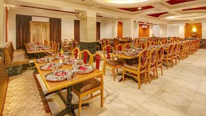 A banquet hall with long tables set for dining, wooden chairs, and a decorative ceiling. - Hotel Yuvraj (Vadodara)