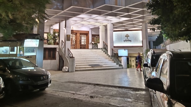 A hotel entrance with a staircase leading to the lobby, a signboard, and parked cars. - Hotel Yuvraj (Vadodara)