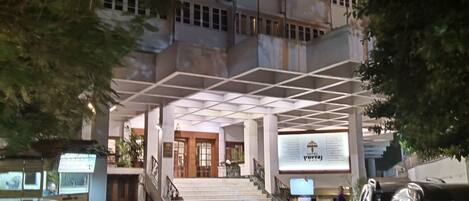 A hotel entrance with a staircase leading to the lobby, a signboard, and parked cars.