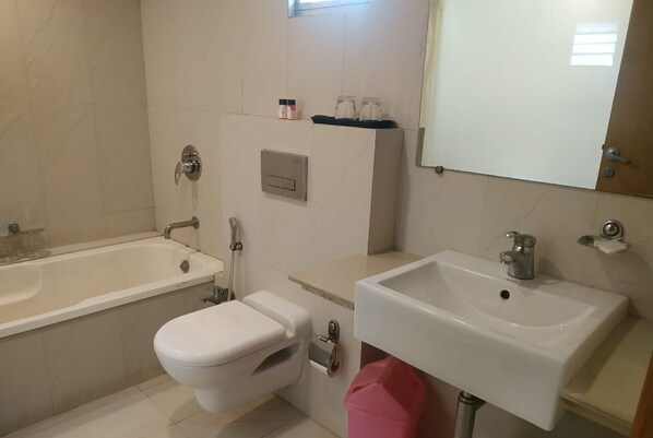 A bathroom with a bathtub, toilet, sink, and a mirror. - Hotel Yuvraj (Vadodara)
