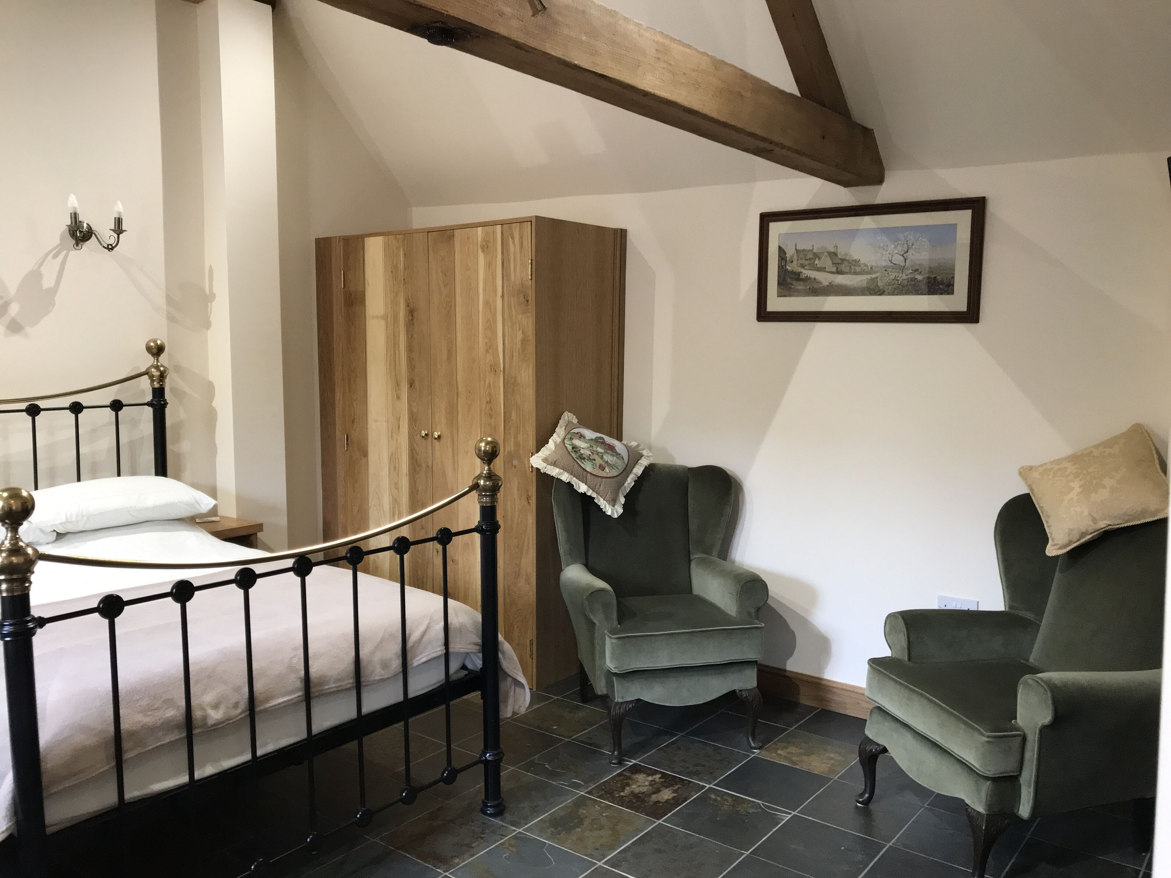 A bedroom with a bed, two armchairs, a wooden wardrobe, and a framed picture on the wall.