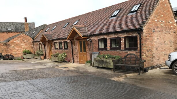 A brick building with a tiled roof, a wooden bench, and a paved courtyard. - Nuneaton - Cottage - Sleeps 2 - Parking - Garden (Nuneaton)
