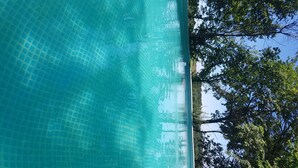 Krystalklart udsyn til en swimmingpool med fliset gulv og træer i baggrunden.