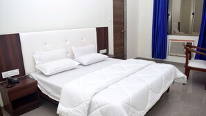 Ein Hotelzimmer mit einem großen Bett, einem Nachttisch aus Holz mit einem Telefon, einem Sessel und einem Spiegel an der Wand.