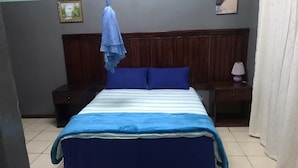Un dormitori amb un llit, dues tauletes de nit, un capçal de llit de fusta, un edredó blau i blanc a ratlles i una safata penjant de color blau.