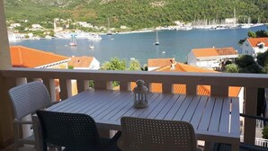 A balcony with a table and chairs overlooking a marina with boats and a coastal town. - Apartments Šišević (Dubrovacko Primorje)